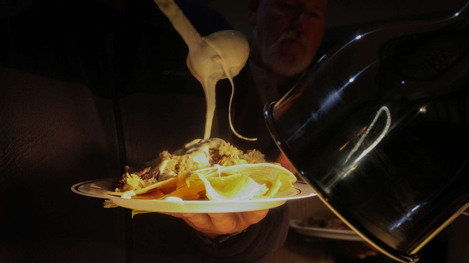 A man is pouring cheese on a plate of food.