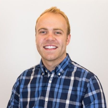 Man with short blond hair smiling, wearing a blue and white plaid shirt.