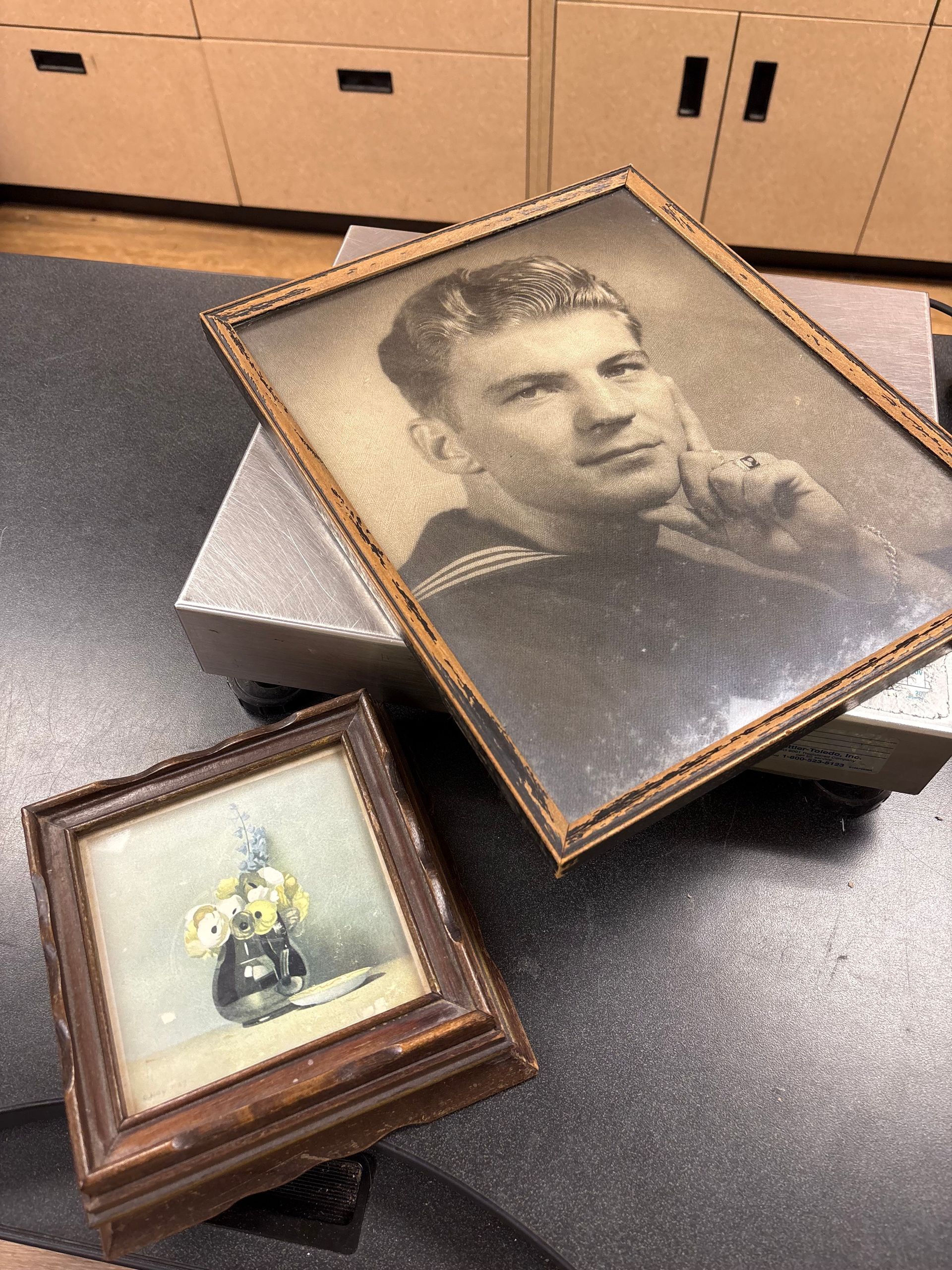 Two framed vintage photos: a sailor in a navy uniform and a small drawing of a figure in a yellow suit.