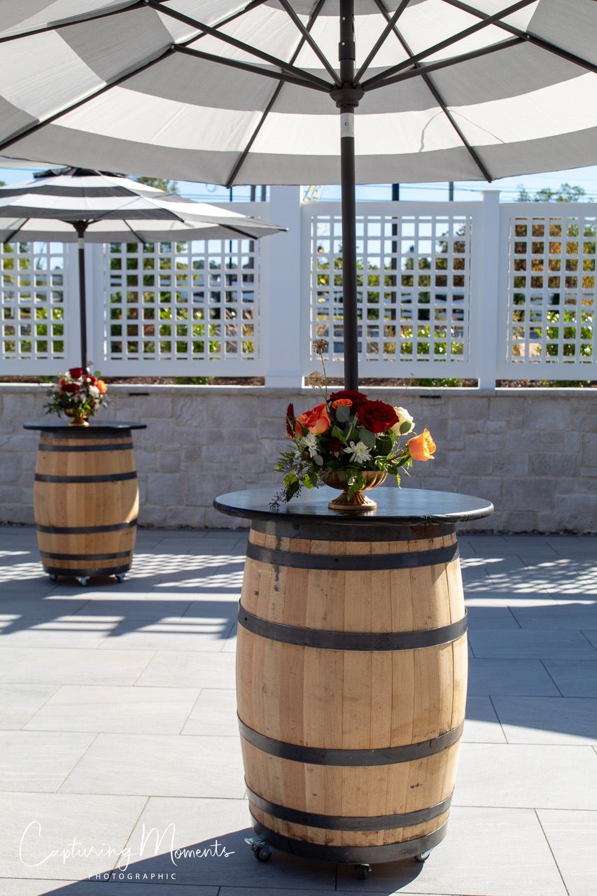 Two wooden barrels with floral arrangements, under striped umbrellas on a patio.