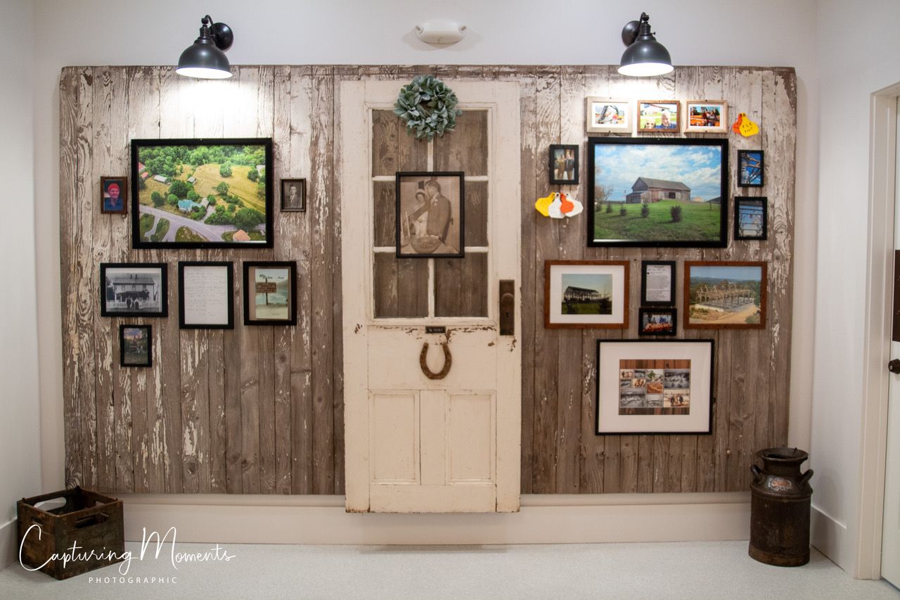 Rustic wall with framed photos, white door, and lamps. Wooden panels and decor create a farmhouse aesthetic.