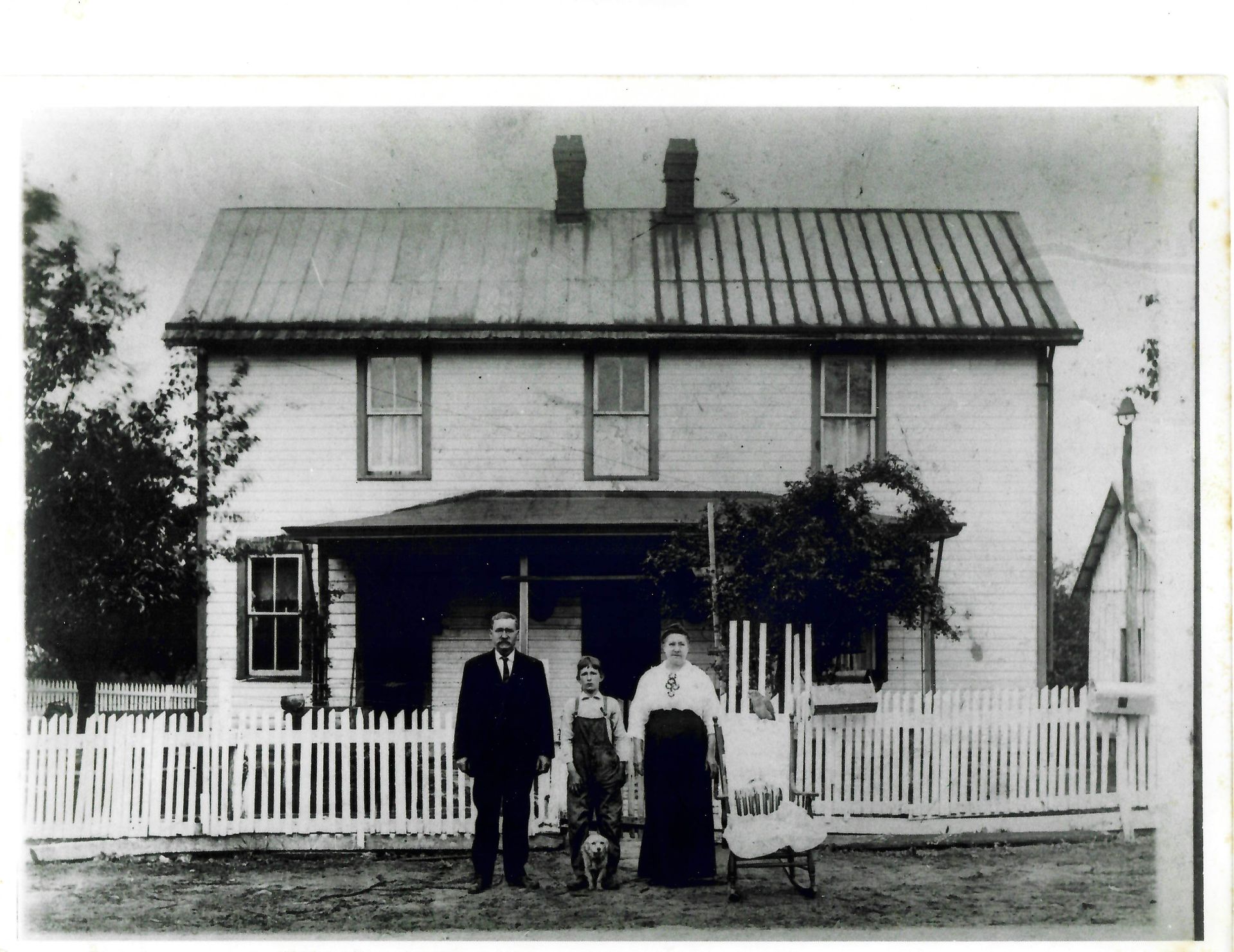 Panoramic view of a town with buildings, a road, and hills. A person stands near a white fence in the foreground.