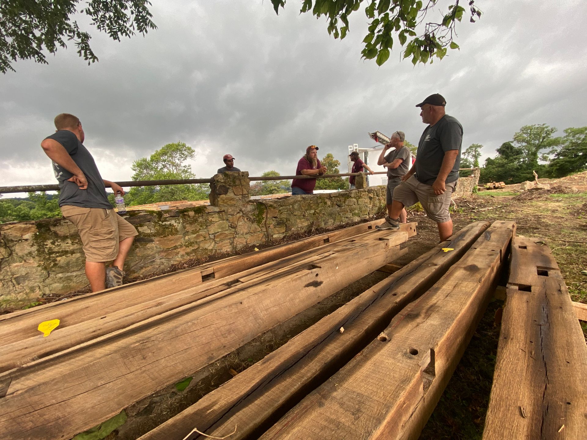 People examining long wooden troughs on a stone structure under a cloudy sky.