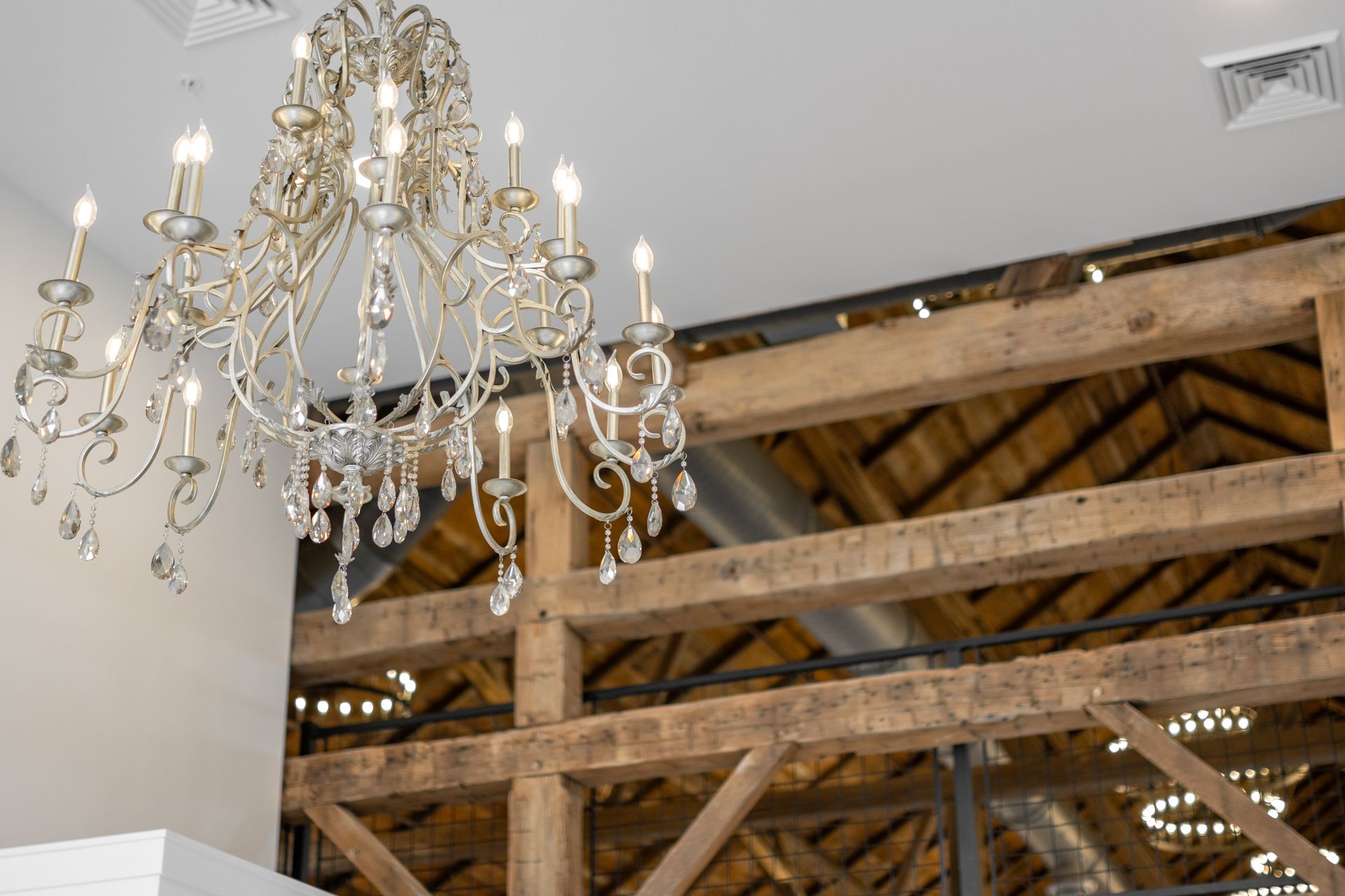 Chandelier hangs in a room with exposed wooden beams and a high ceiling.