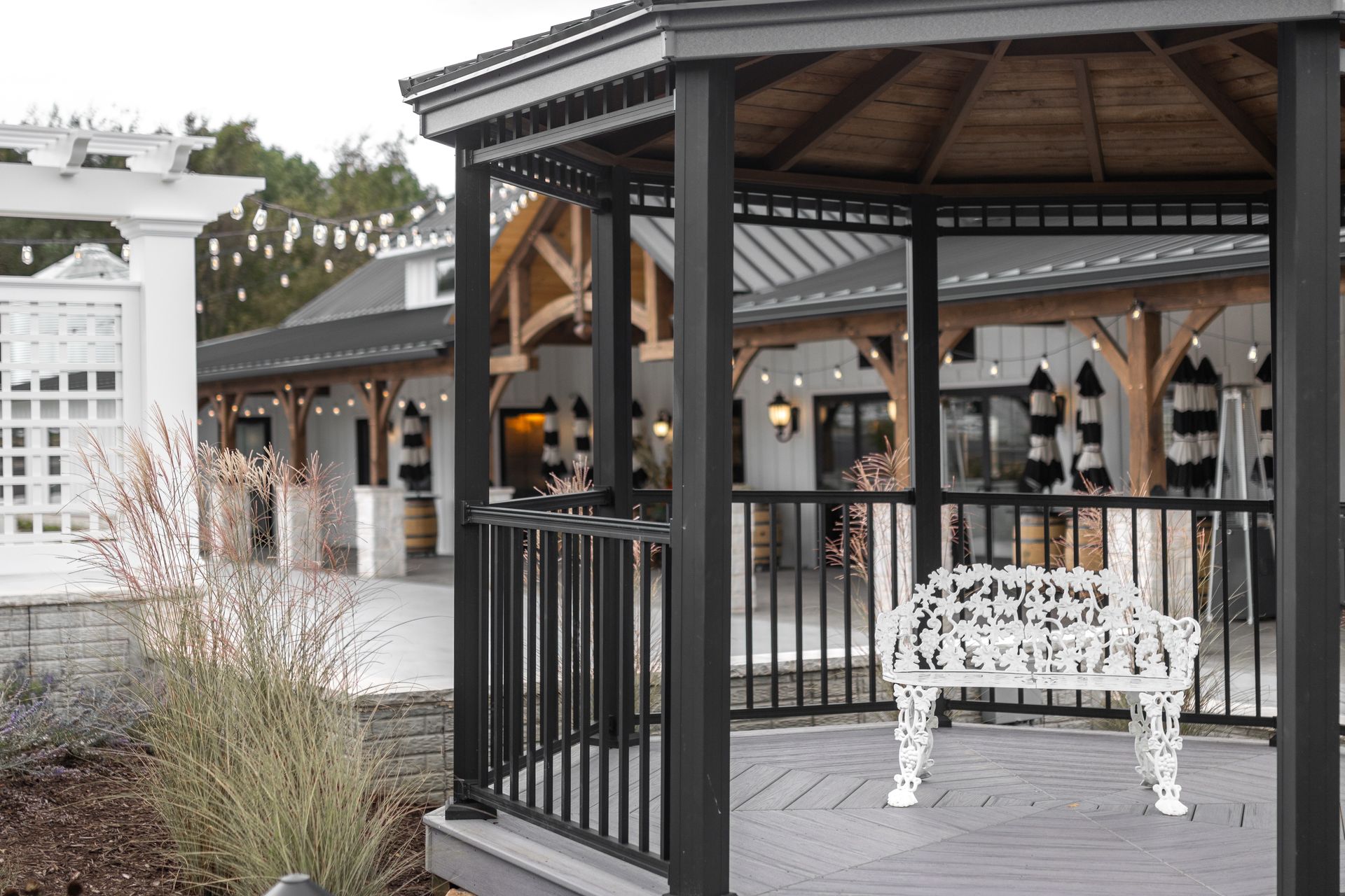 Gazebo with black trim, a white bench, and a building in the background.