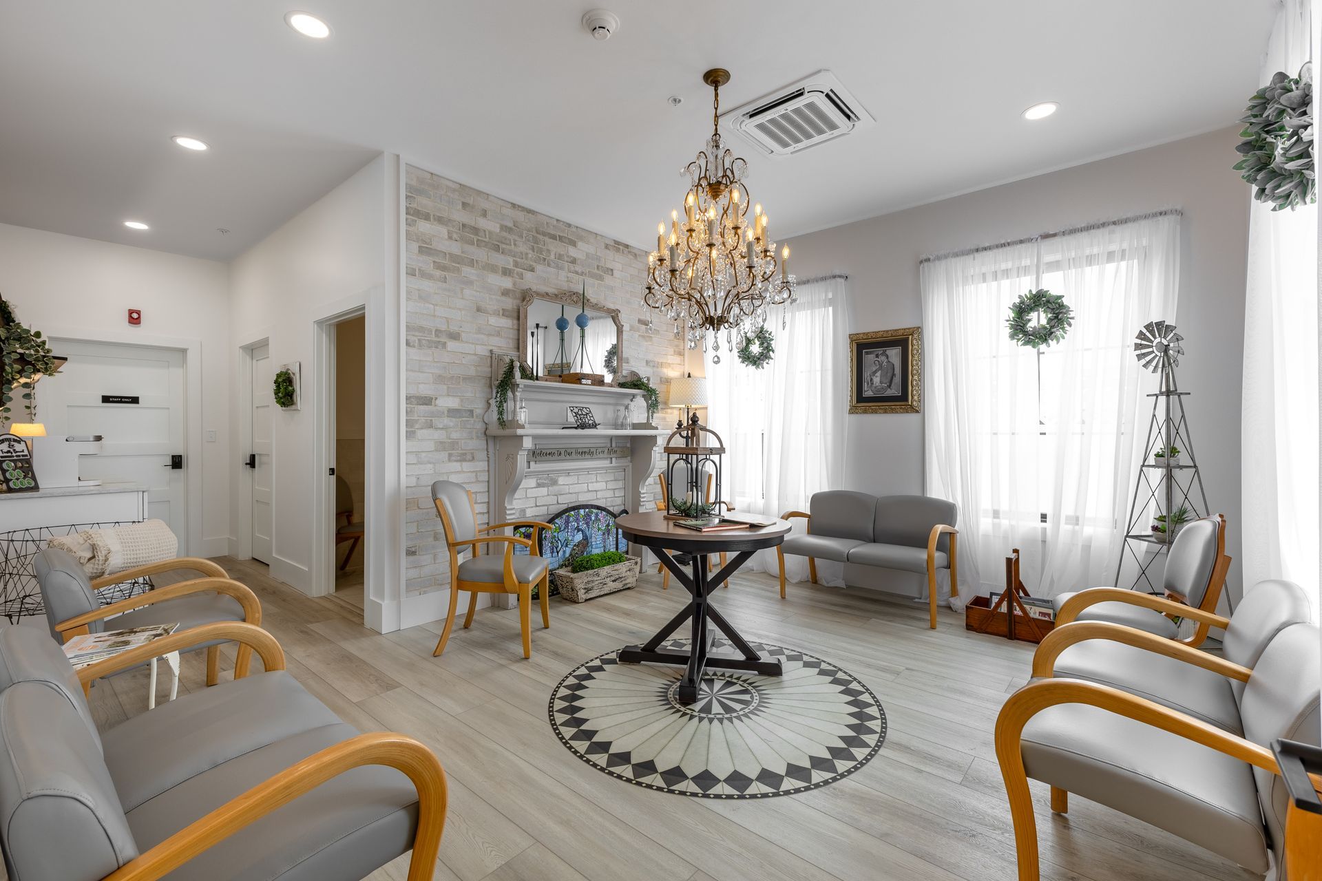 In Law Suite with gray chairs, chandelier, fireplace, and decorated windows.