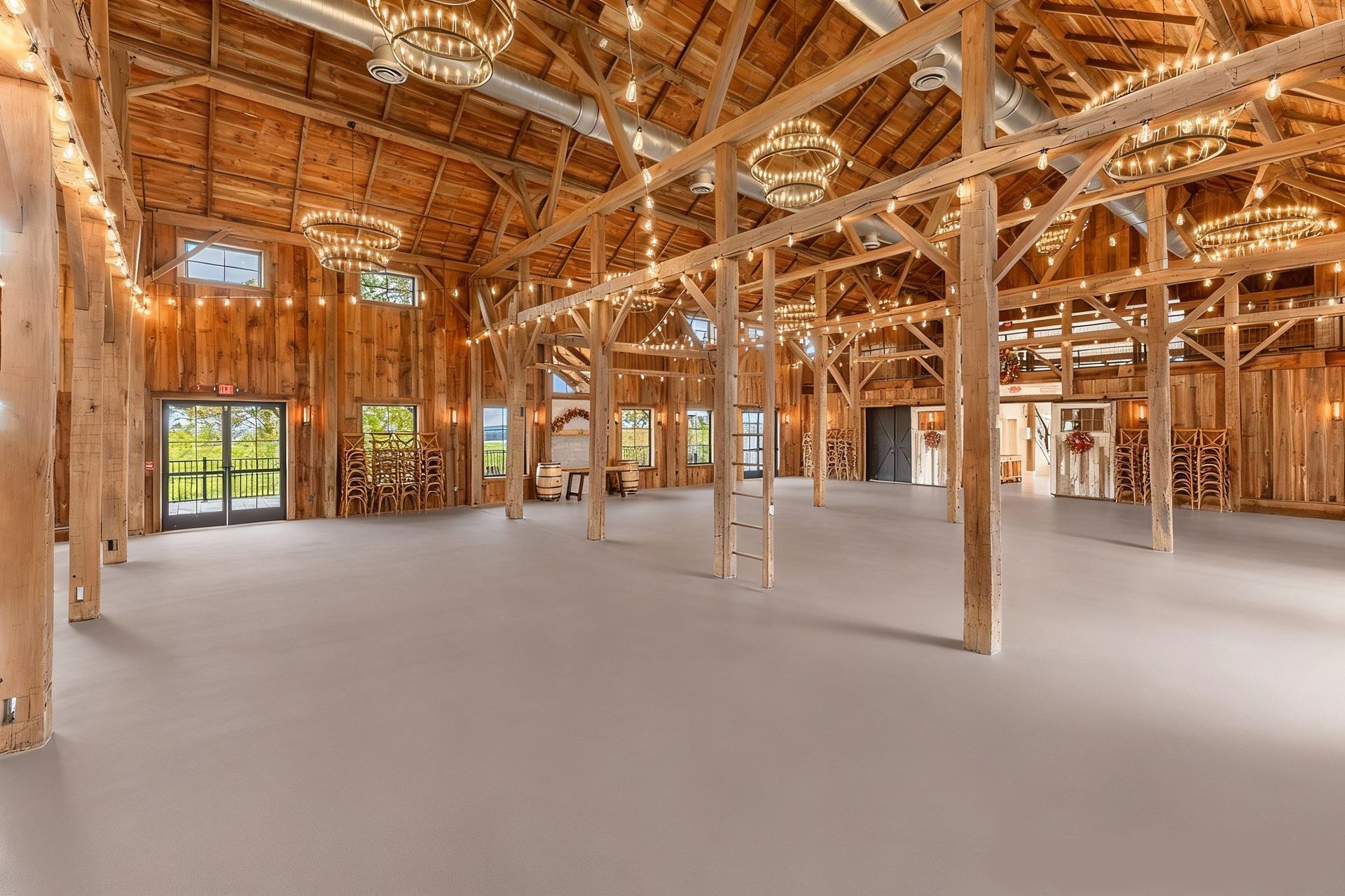 Spacious barn interior with wood beams, gray floor, string lights, and chandeliers.