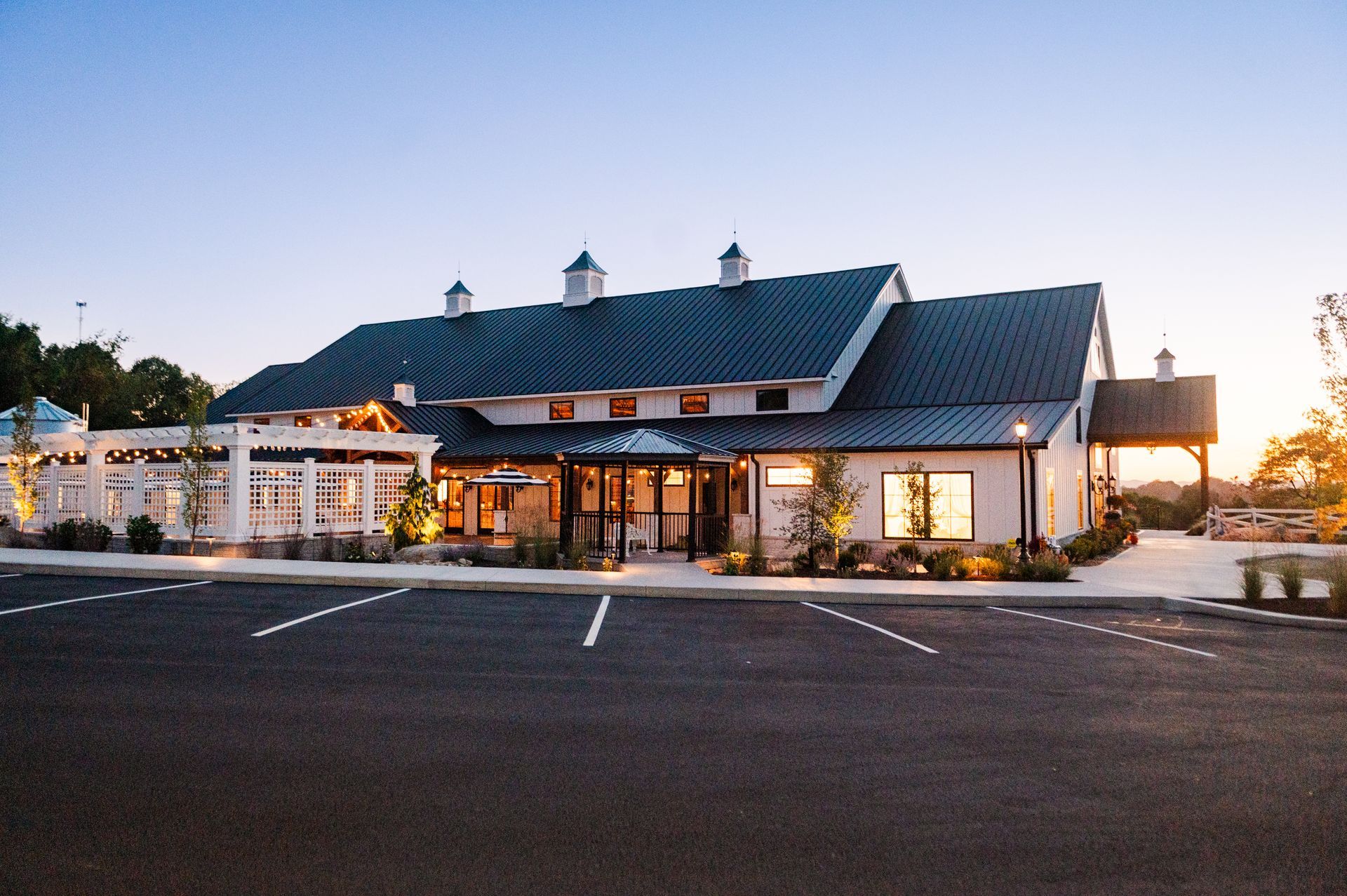Modern white reclaimed antique barn wedding venue with a dark roof and a parking lot. Dusk lighting. Morgantown, Masontown