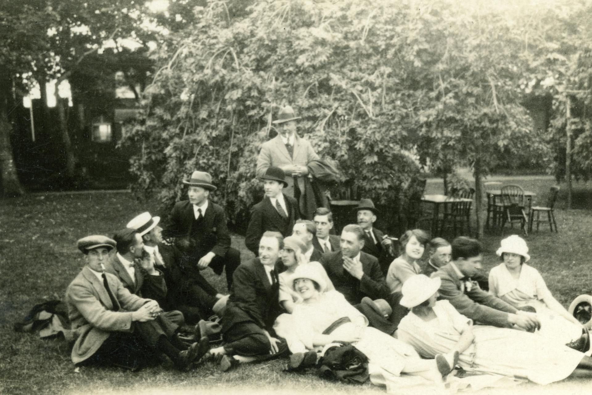 Group of people sitting on grass under a tree, possibly for a picnic.