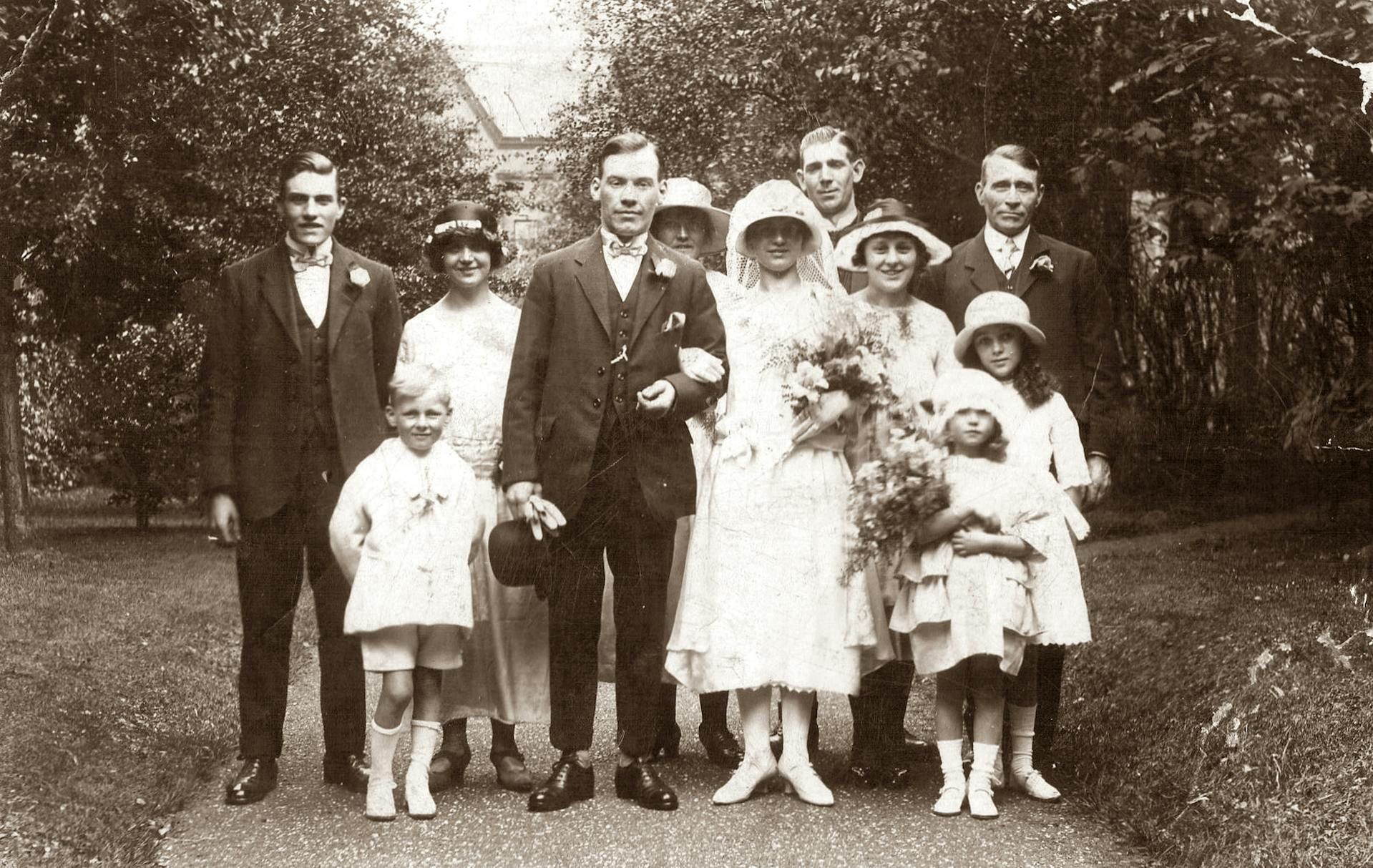 Wedding party posing outdoors. Couple center, surrounded by attendants. Formal attire.