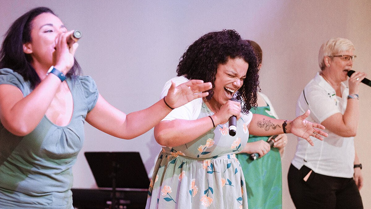 A group of women are singing into microphones on a stage.