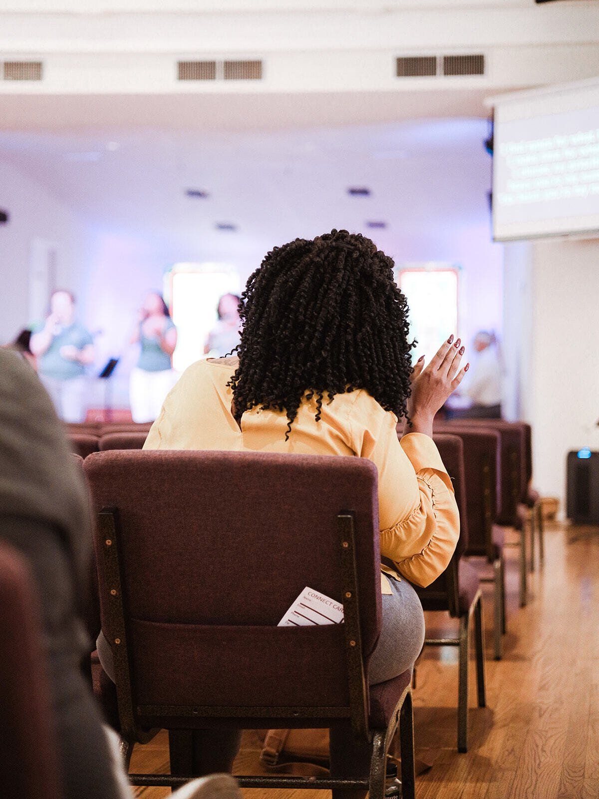 A woman is sitting in a chair in a church with her hands in the air.
