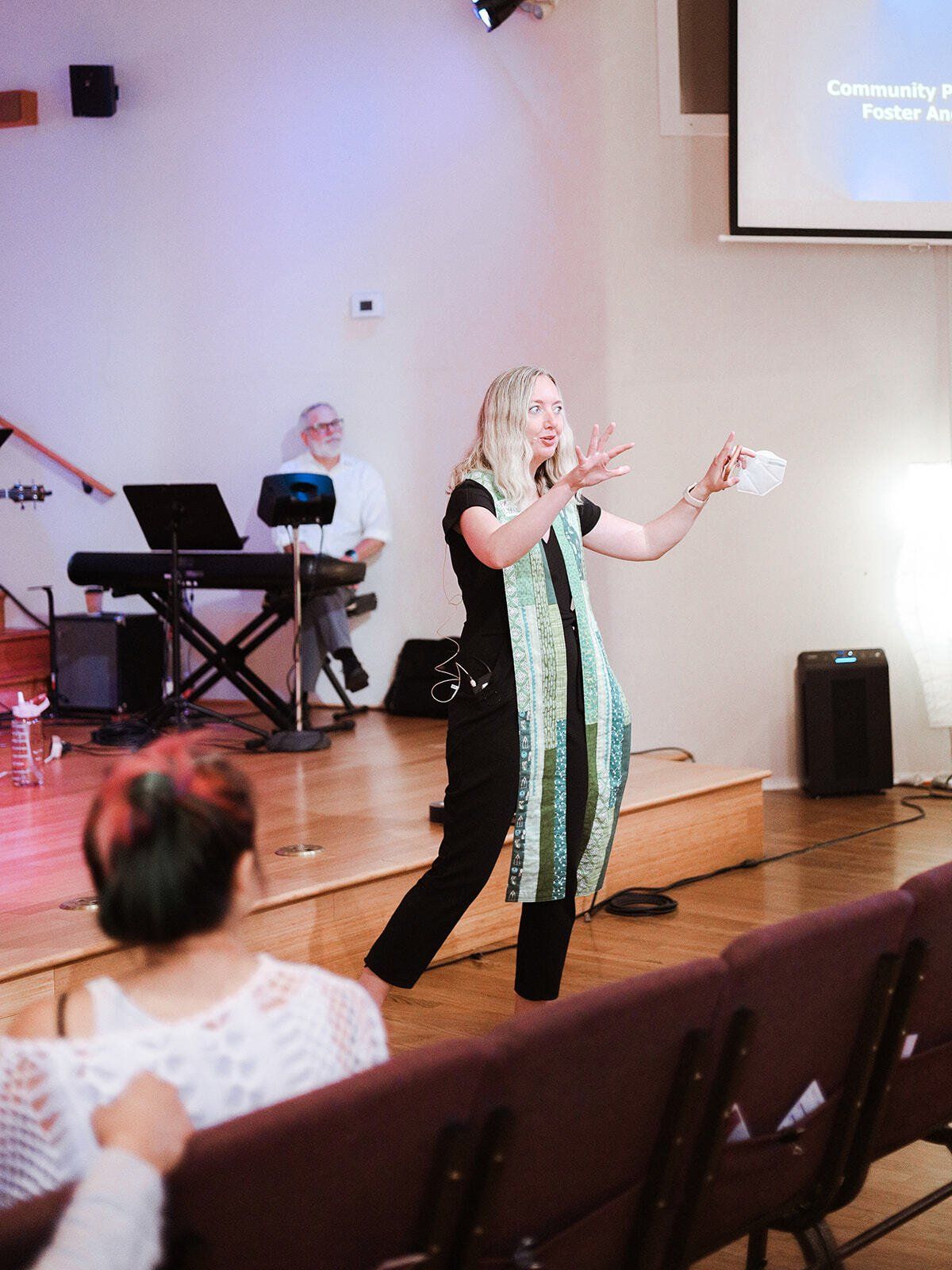 A woman is standing on a stage in front of a projector screen.