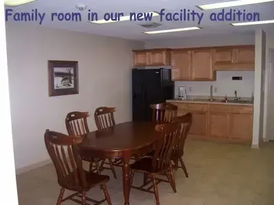 Family room in new facility: dining table with chairs, kitchen with cabinets, refrigerator.