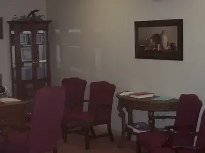Waiting room with burgundy chairs, a curio cabinet, and a small table with books.