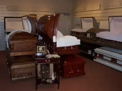 A display of various open and closed wooden caskets inside a funeral home, lit with warm lighting.