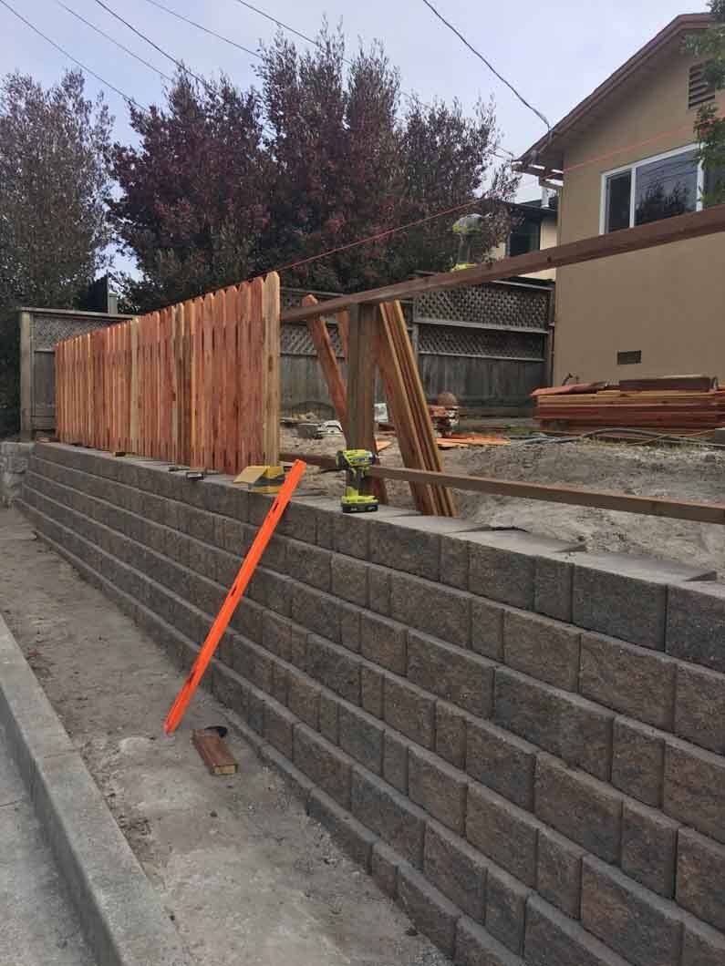 A brick wall is being built next to a wooden fence.
