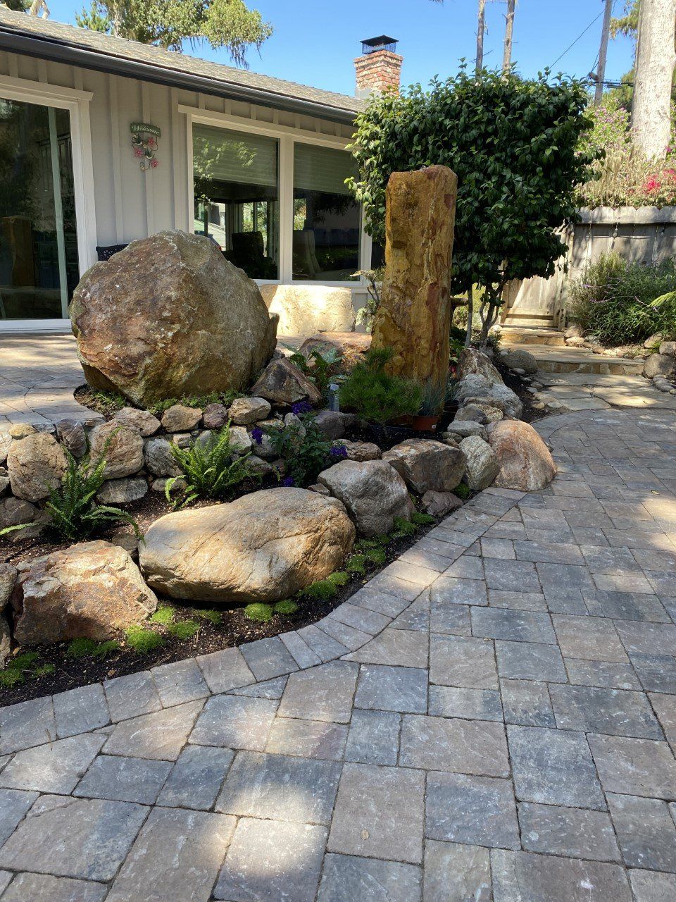 A stone walkway leading to a house with a large rock in the middle.