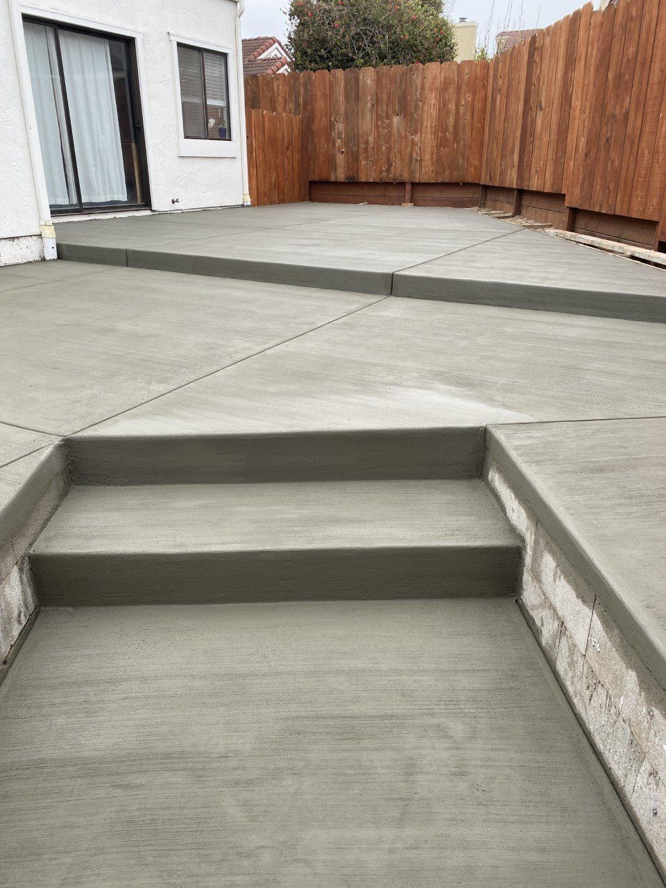 A concrete patio with stairs and a wooden fence in the background.