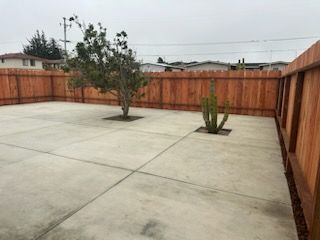 A concrete patio with a wooden fence and a tree in the middle.