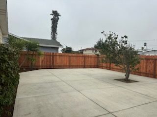 A concrete patio with a wooden fence and a tree in the middle.