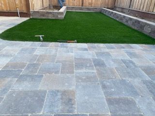A patio with a lawn and a fence in the background.