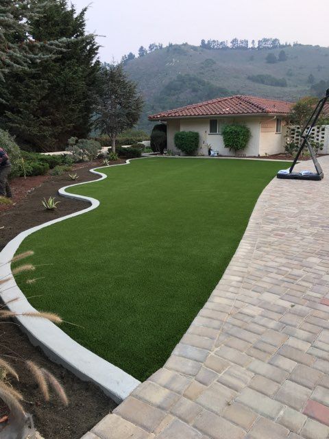 A brick walkway leading to a house with a lush green lawn