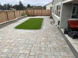 A patio with a lawn and a fence in the backyard of a house.