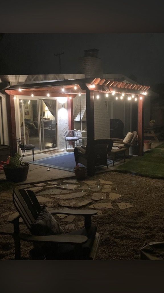 A patio with a pergola and chairs at night.