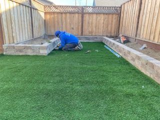 A man is kneeling on the grass in a backyard.