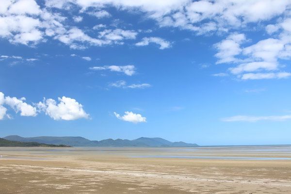 A Beach With Mountains in the Background and a Blue Sky With Clouds — Coastal Arborist Services in Whitsundays, QLD