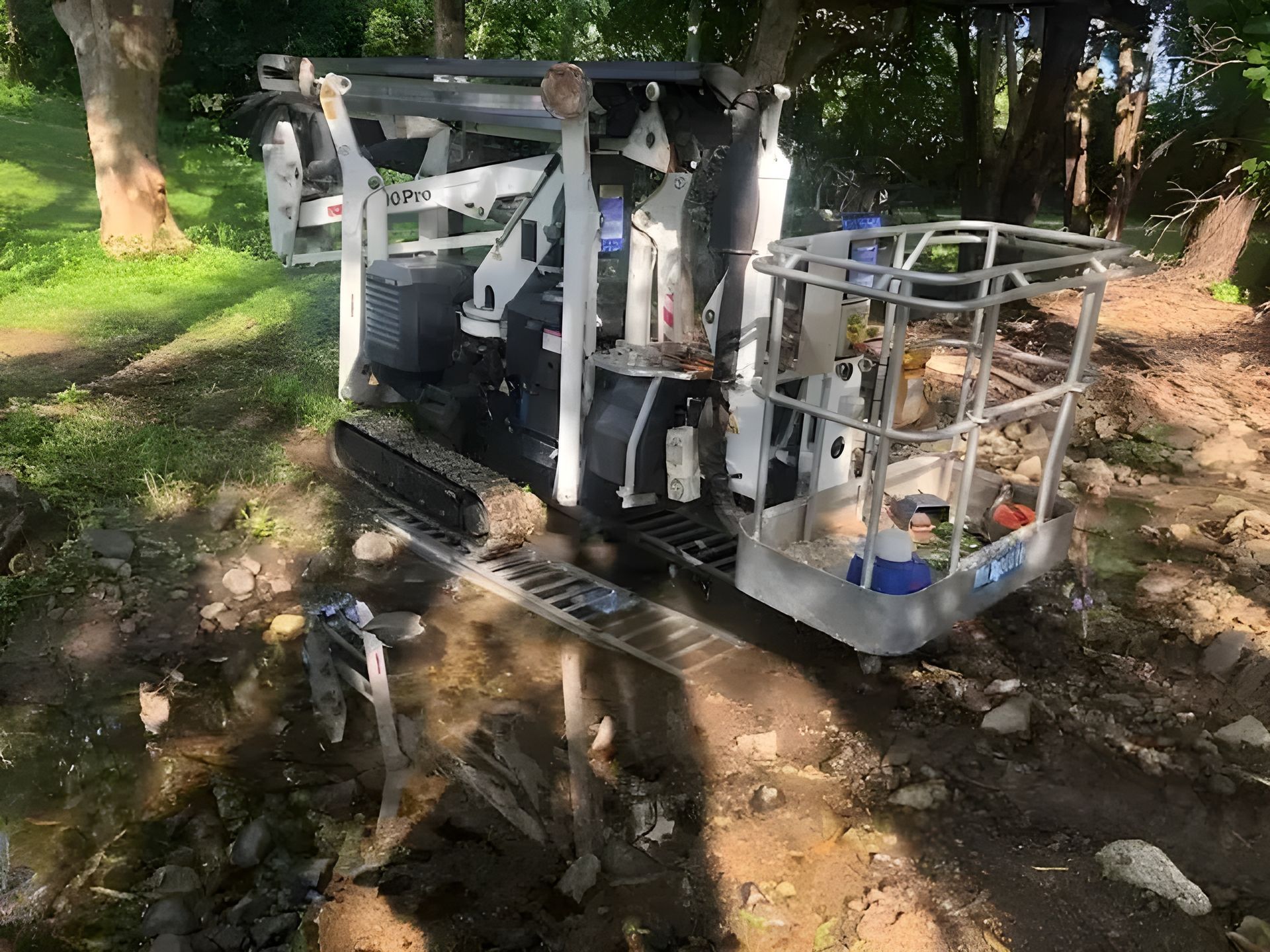 A Bucket Lift is Sitting in the Dirt Next to a Tree — Coastal Arborist Services in Cannonvale, QLD