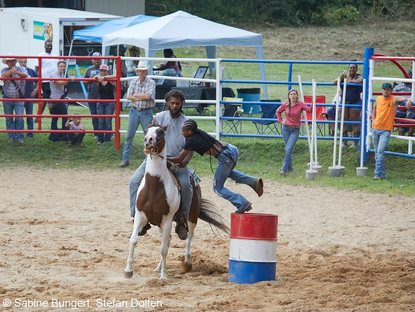 A man is riding a horse around a red white and blue barrel