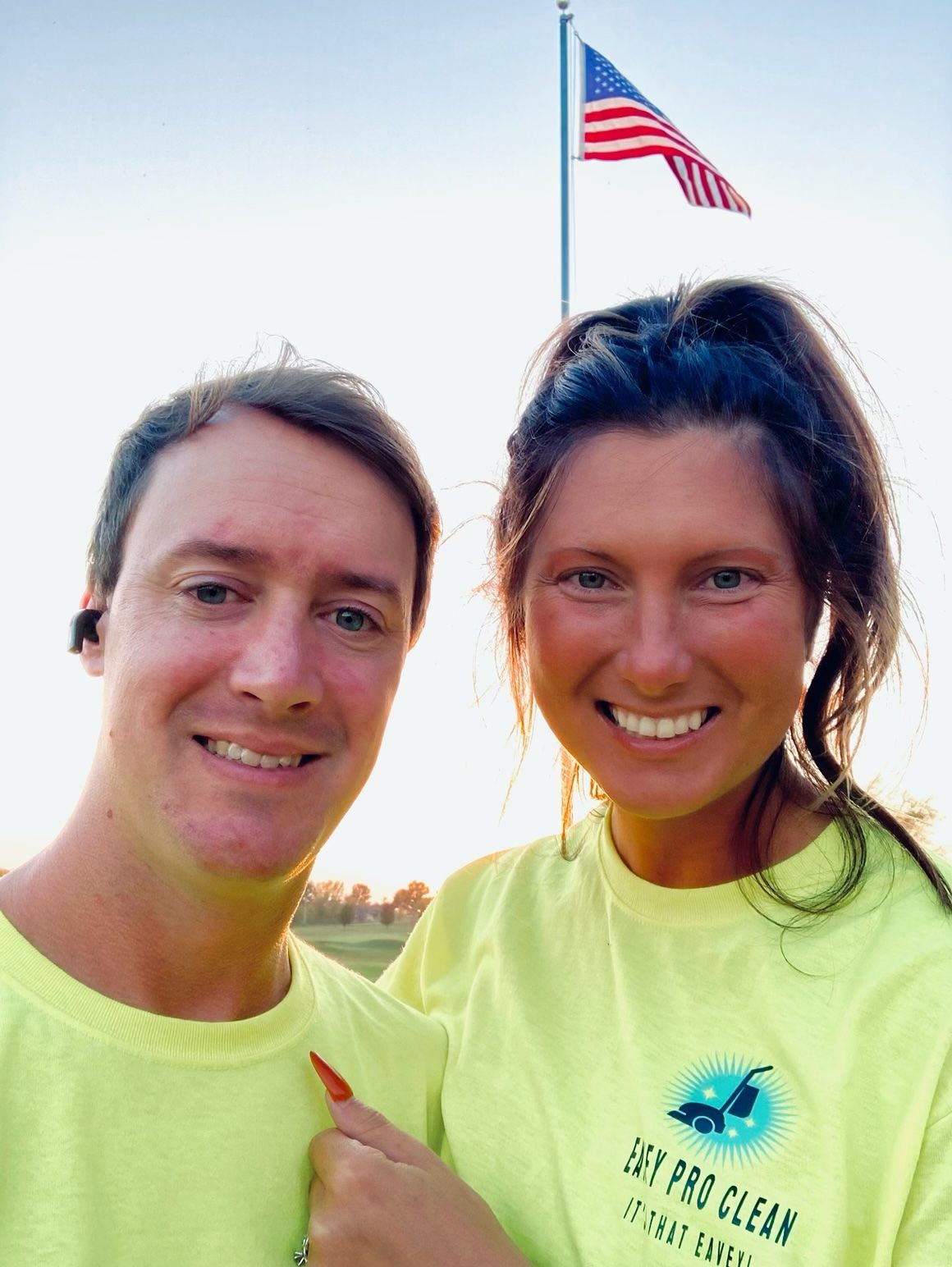 A man and a woman are posing for a picture in front of an american flag.