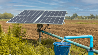 A solar panel is sitting on top of a water pump in a field.