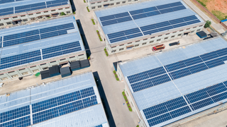 An aerial view of a warehouse with lots of solar panels on the roofs.