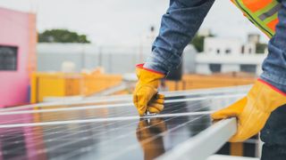 A man wearing yellow gloves is working on a solar panel.