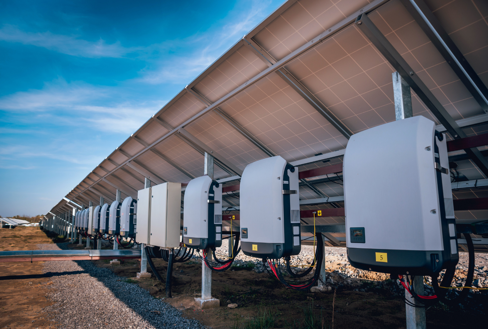 A row of solar panels and inverters in a solar farm.