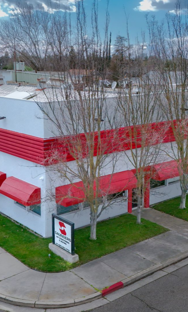 Building with white walls, red awnings, and a sign. Bare trees in front; overcast sky.