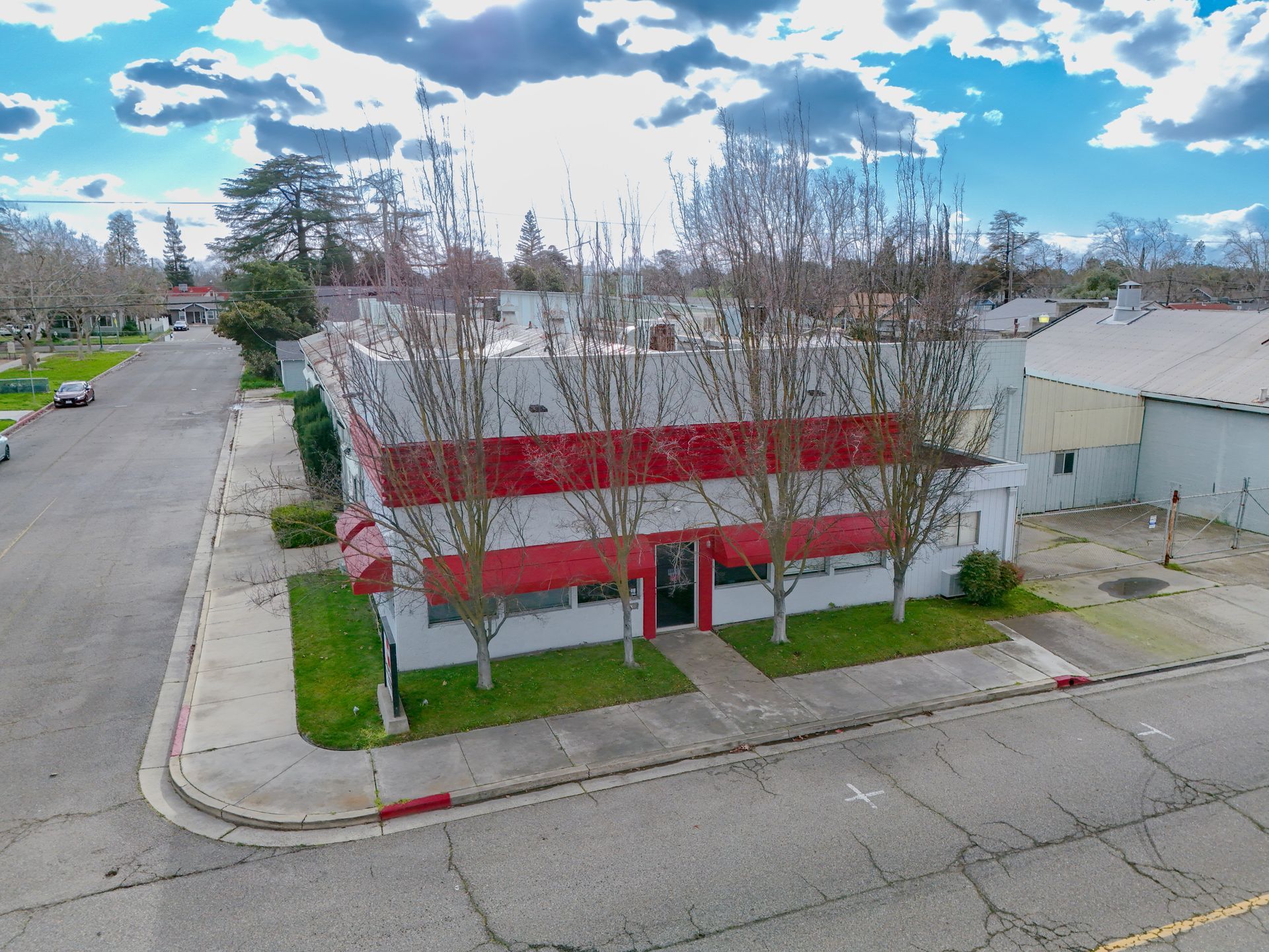 Two-story commercial building with red stripes, trees, and cloudy sky.