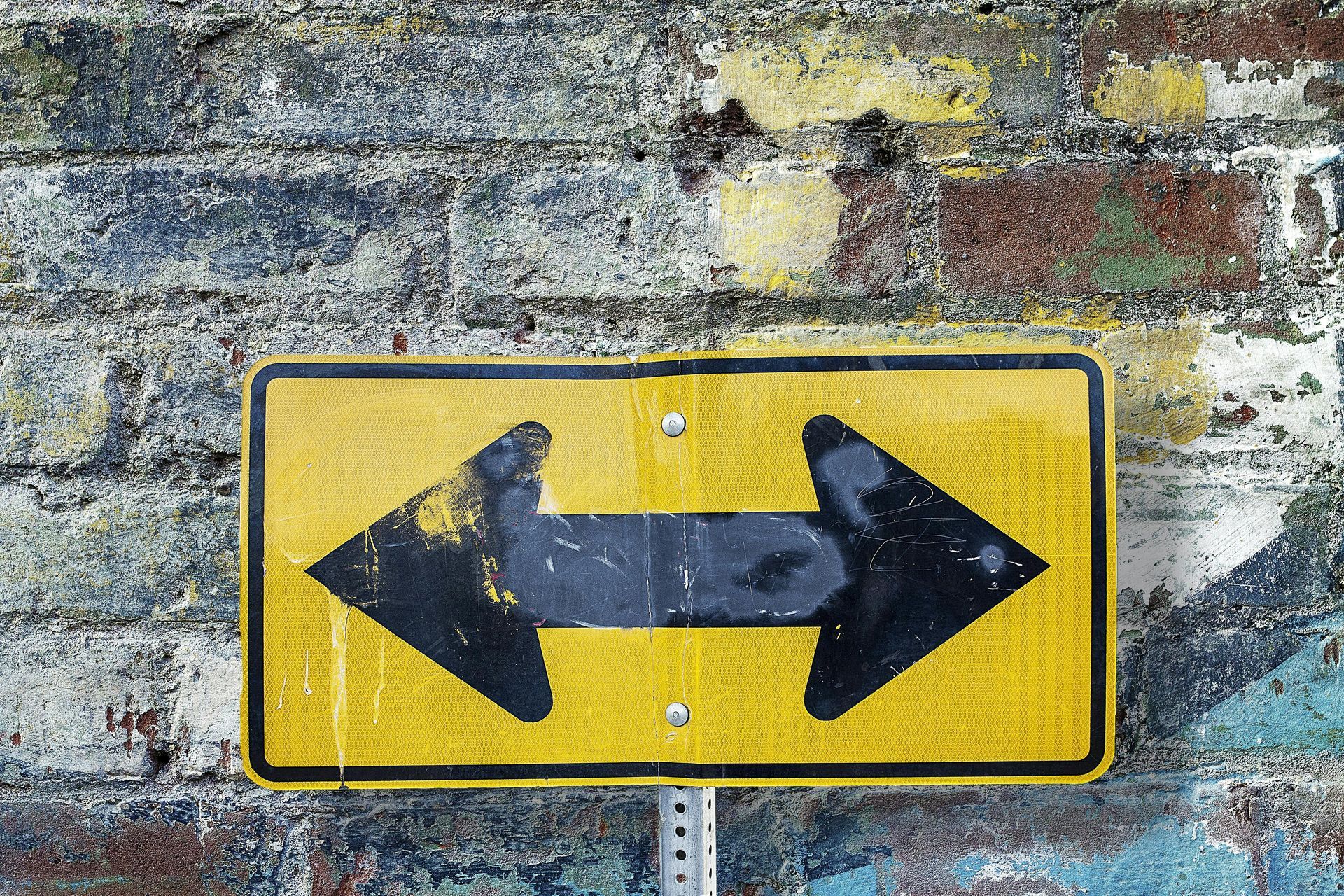 Yellow sign with black double arrow on a brick wall.