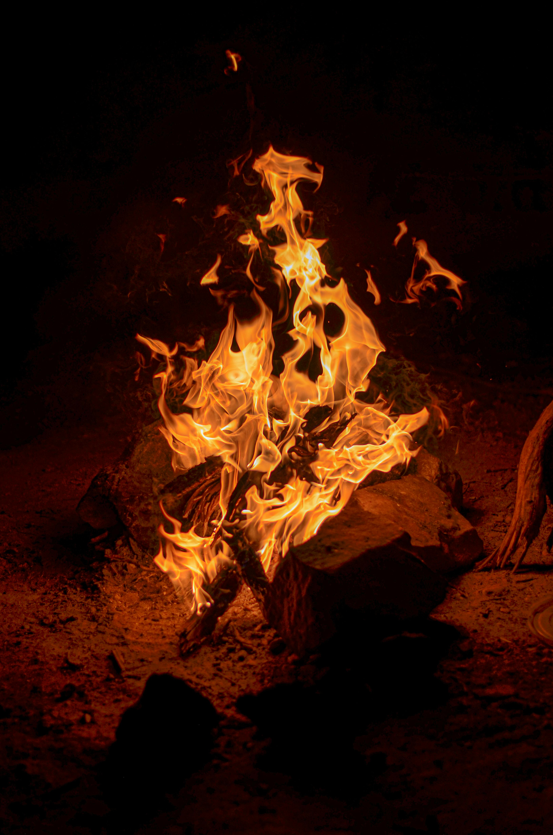Burning bonfire with orange and yellow flames against a dark background.