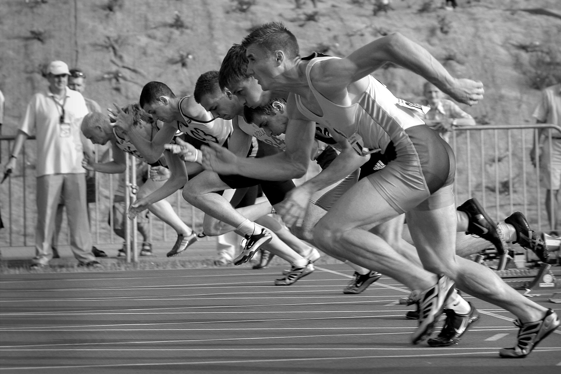Sprinters at the starting line, poised to run a race. They are on a track in a daytime setting.