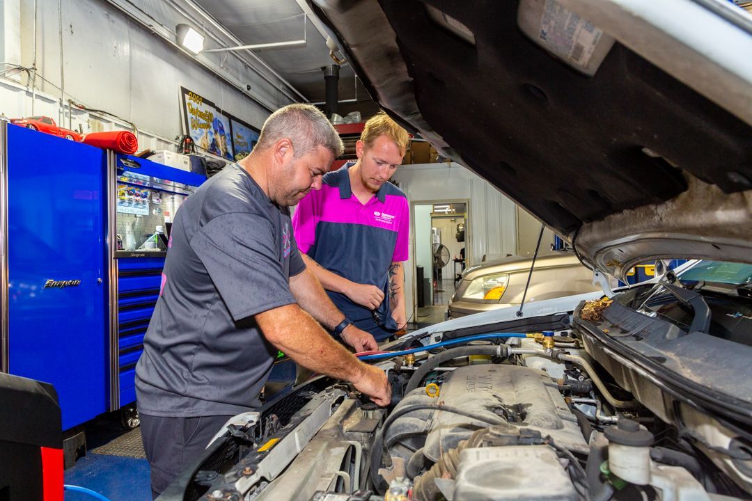 Two men are working on a car engine in a garage.