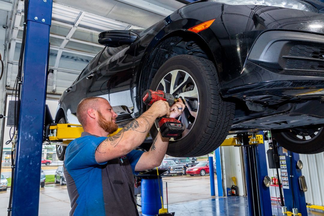 A man is working on a car on a lift in a garage.