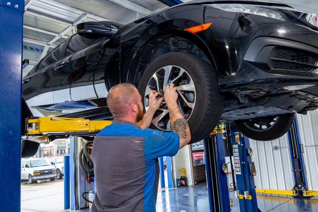 A man is working on a car on a lift in a garage.