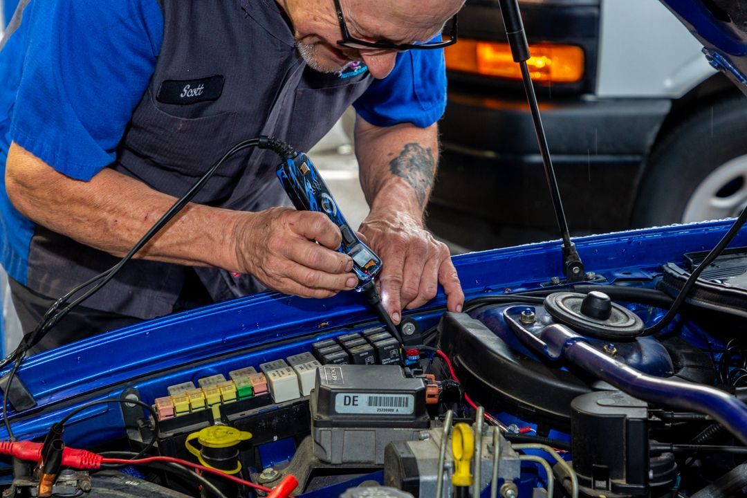 A man is working on the engine of a blue car.
