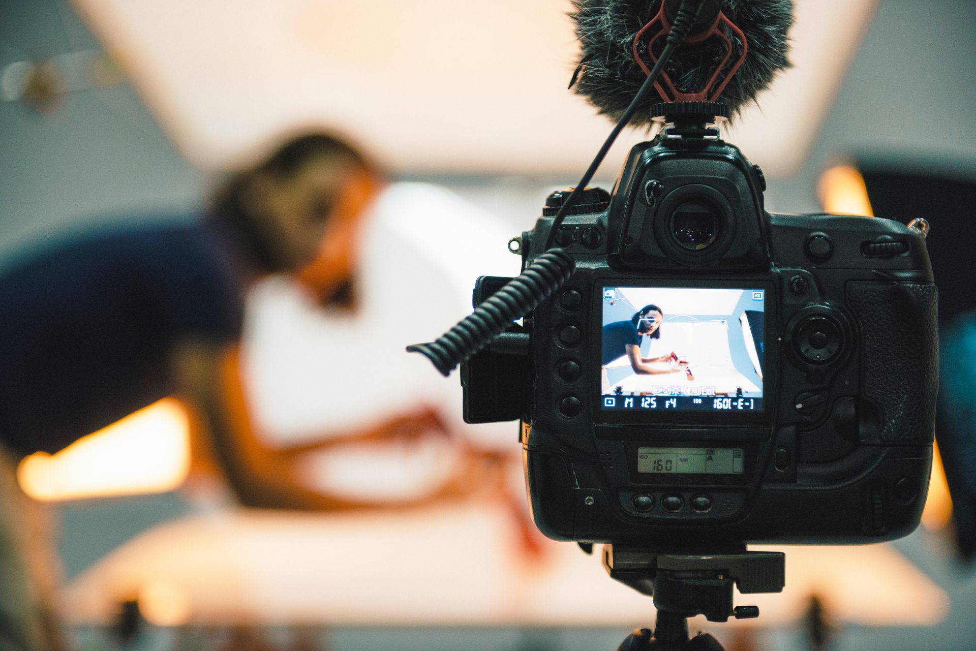 A camera is taking a picture of a woman laying on a bed.