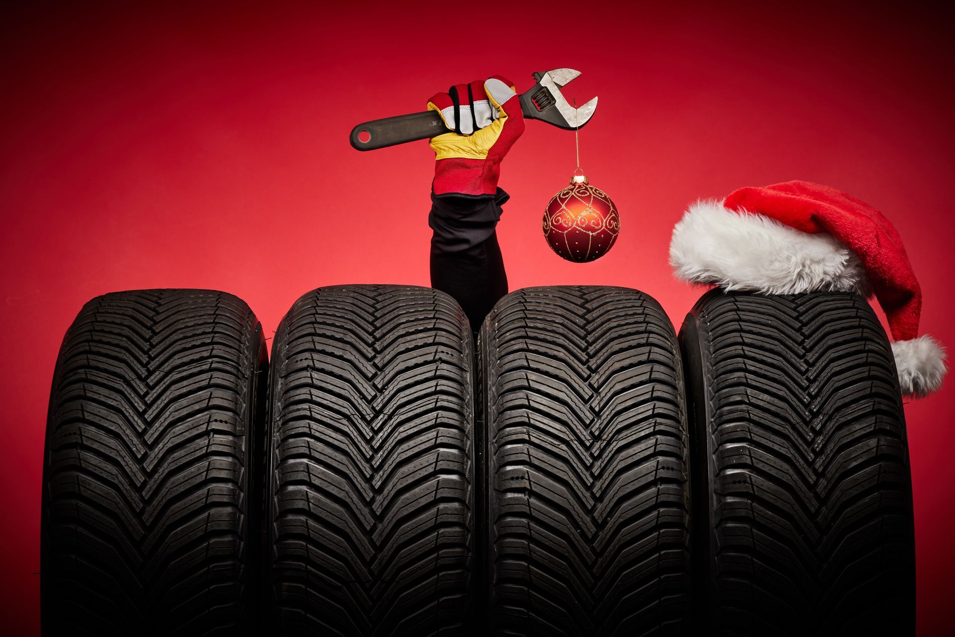 Row of car tires with a hand holding a wrench and a Christmas ornament, wearing a Santa hat