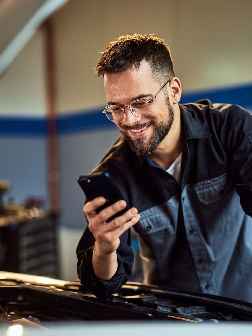 A man is looking at his cell phone while working on a car.